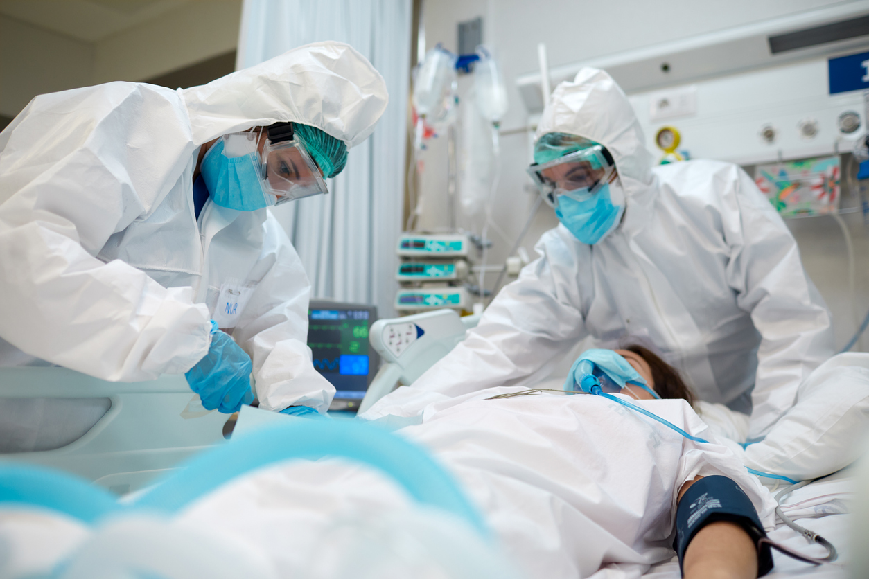 Two healthcare workers wearing full protective gear care for an intubated patient in the ICU who is suffering from COVID.