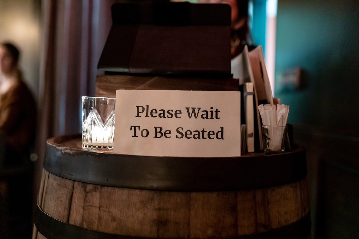 Posted sign on a hostess stand read " Please Wait to be seated"