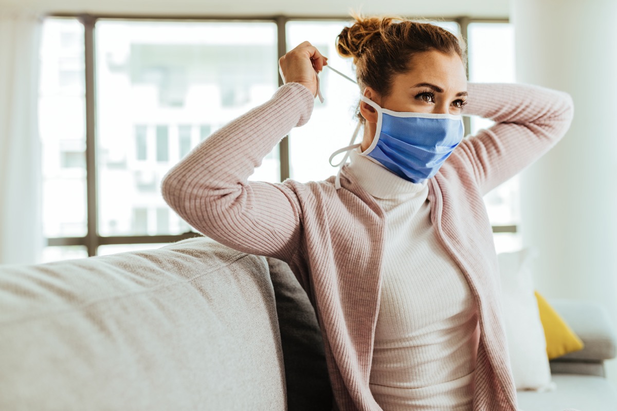Young woman using protective face mask at home during coronavirus pandemic.