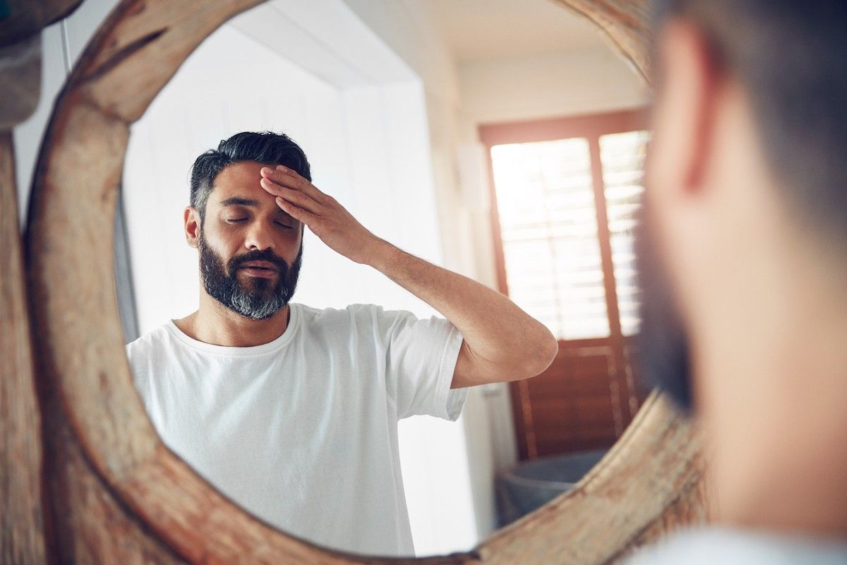  Photo d'un homme debout devant le miroir de la salle de bain, l'air épuisé, se tenant la tête 