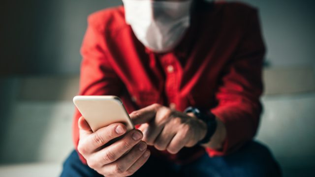 man using phone at home while wearing a mask