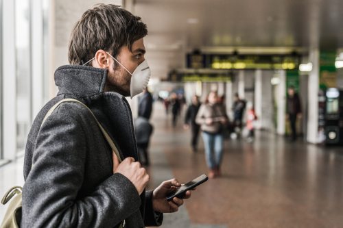 Man wearing protective mask to prevent Coronavirus and using mobile phone in airport terminal