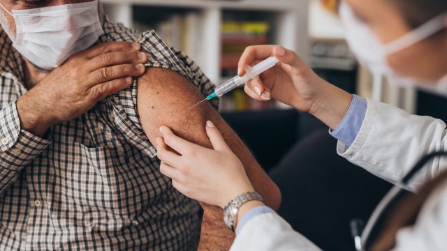 A senior man receives a COVID-19 vaccine injection in his arm from a healthcare worker.