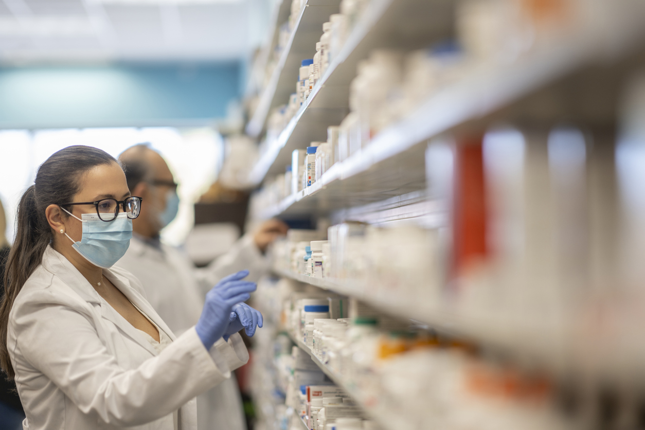 A pharmacist wearing a face mask stocks medicines on a shelf