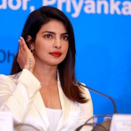 priyanka chopra in a white suit sitting at a desk