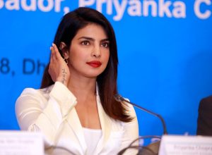 priyanka chopra in a white suit sitting at a desk
