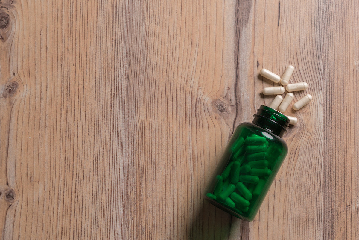 Probiotics spilled out from green bottle on wooden surface