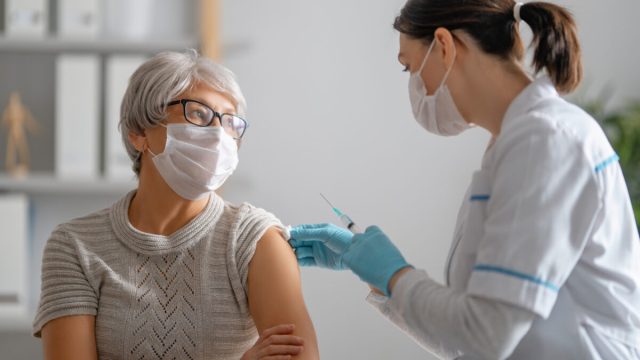 A senior woman wearing a face mask receives a COVID-19 vaccine from a female doctor.