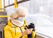 woman in winter clothing with face mask on a bus looking at her phone