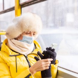woman in winter clothing with face mask on a bus looking at her phone