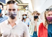 group walking with serious face expression at railway station - New normal travel concept with young people covered by protective mask - Focus on blond girl with hat