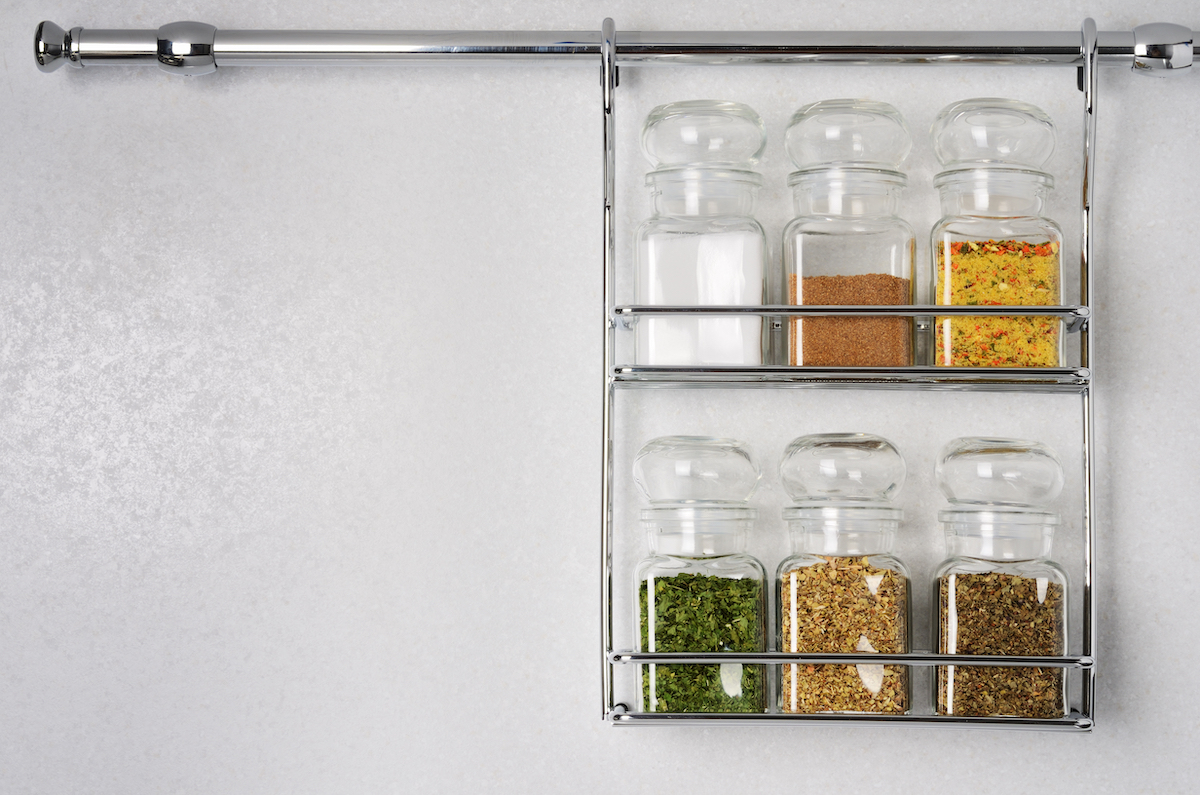 Bottles with spices and seasonings hanging on rack against white background