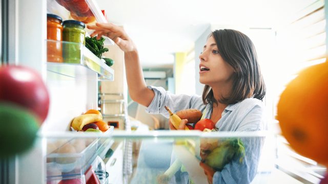 Shot from inside the fridge of a young woman picking some fruit and veggies from the fridge