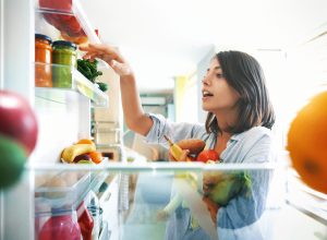 Shot from inside the fridge of a young woman picking some fruit and veggies from the fridge