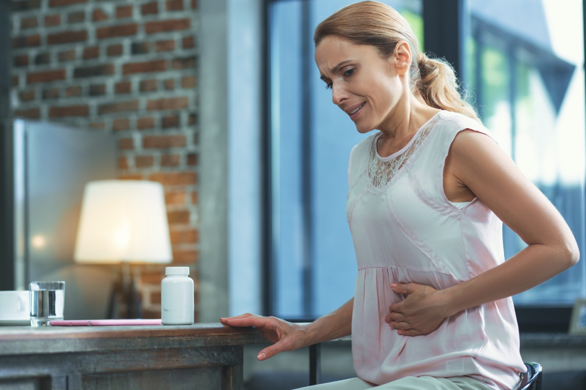 woman in white shirt holding stomach under ribs as if in pain