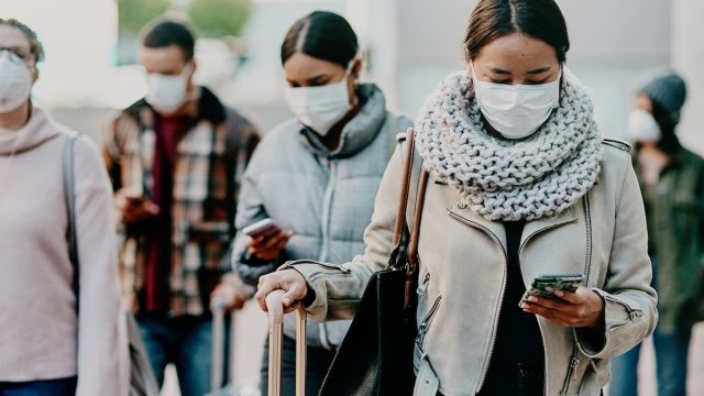 Shot of a young woman using a smartphone and wearing a mask while traveling