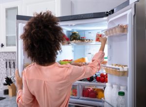woman in pink shirt with dark curly hair opening double door fridge