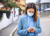 Woman with face protection mask texting on mobile in the street