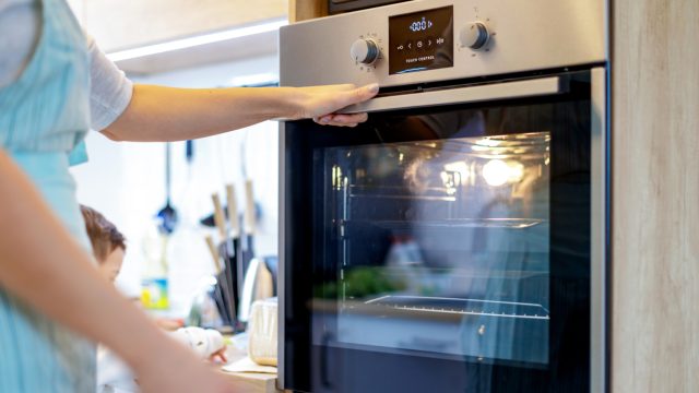 A woman wearing a blue apron turns on the oven in her kitchen