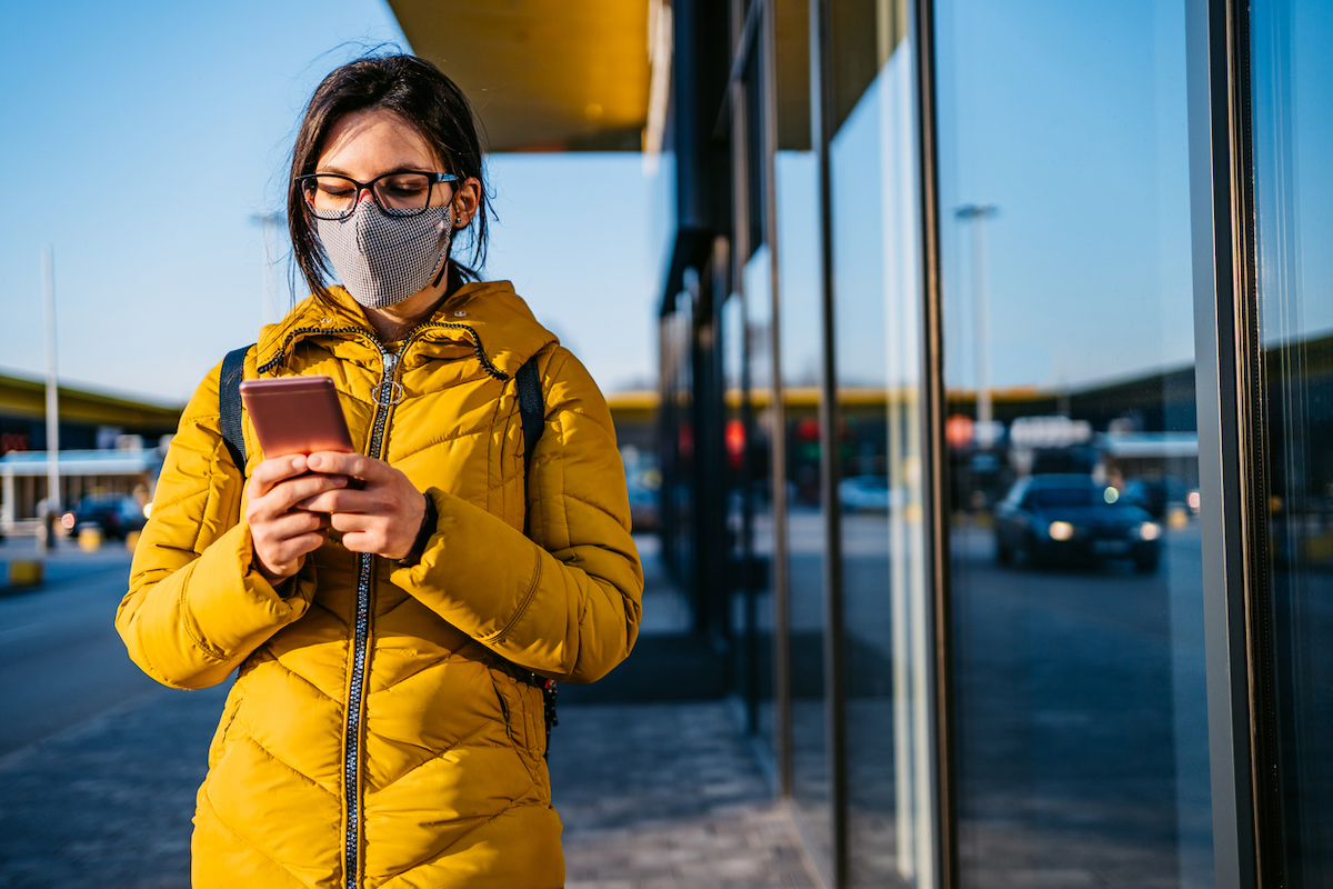 Young woman using smartphone while wearing a mask in time of the COVID pandemic