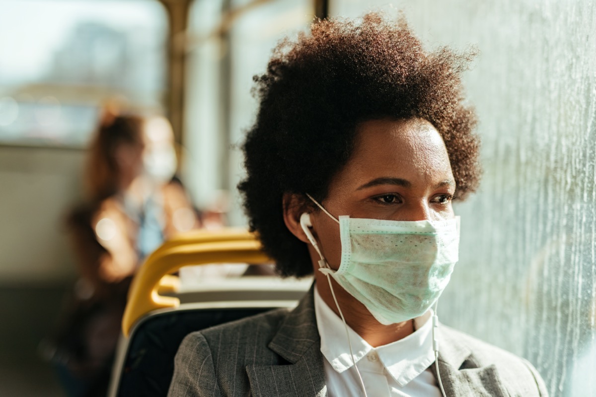 young woman wearing surgical mask and apple headphones on public bus