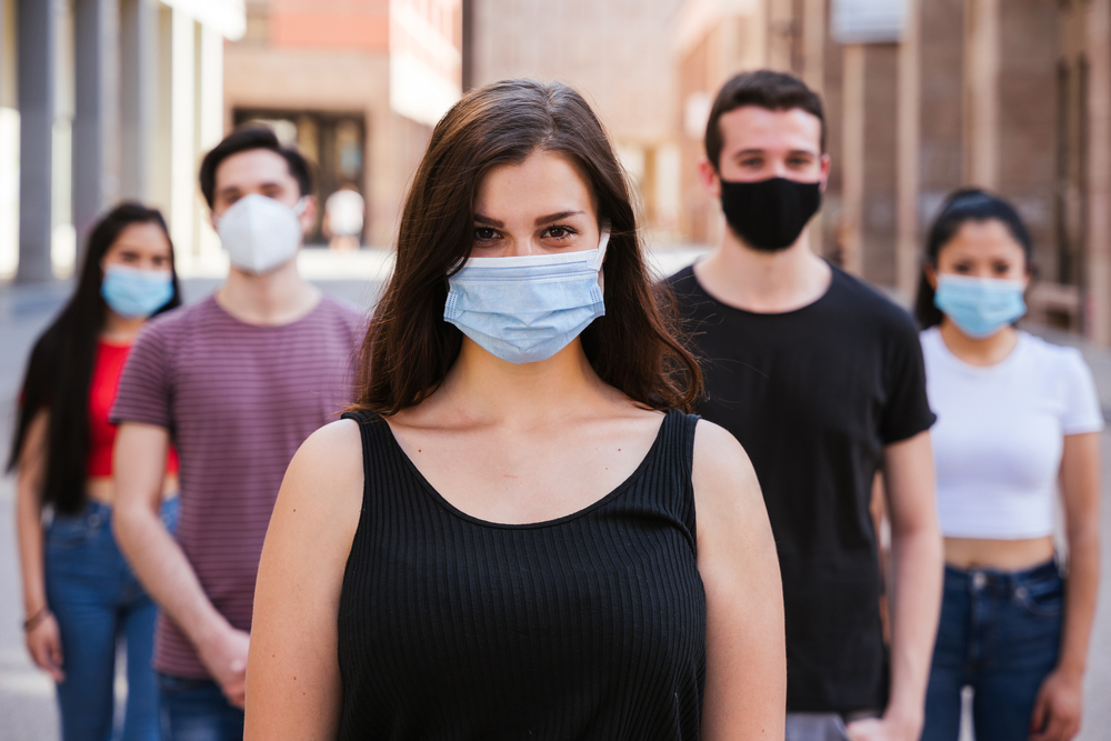 A group of young people wearing face masks stand spread out in an alleyway.