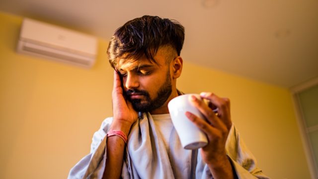 young man with beard holding tea and indicating a headache
