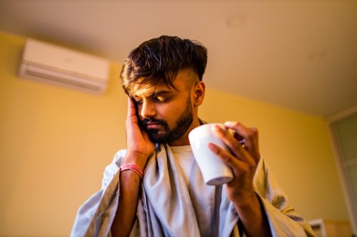 young man with beard holding tea and indicating a headache