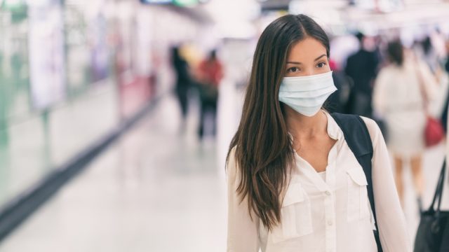A young woman walks through a train station while wearing a face mask.