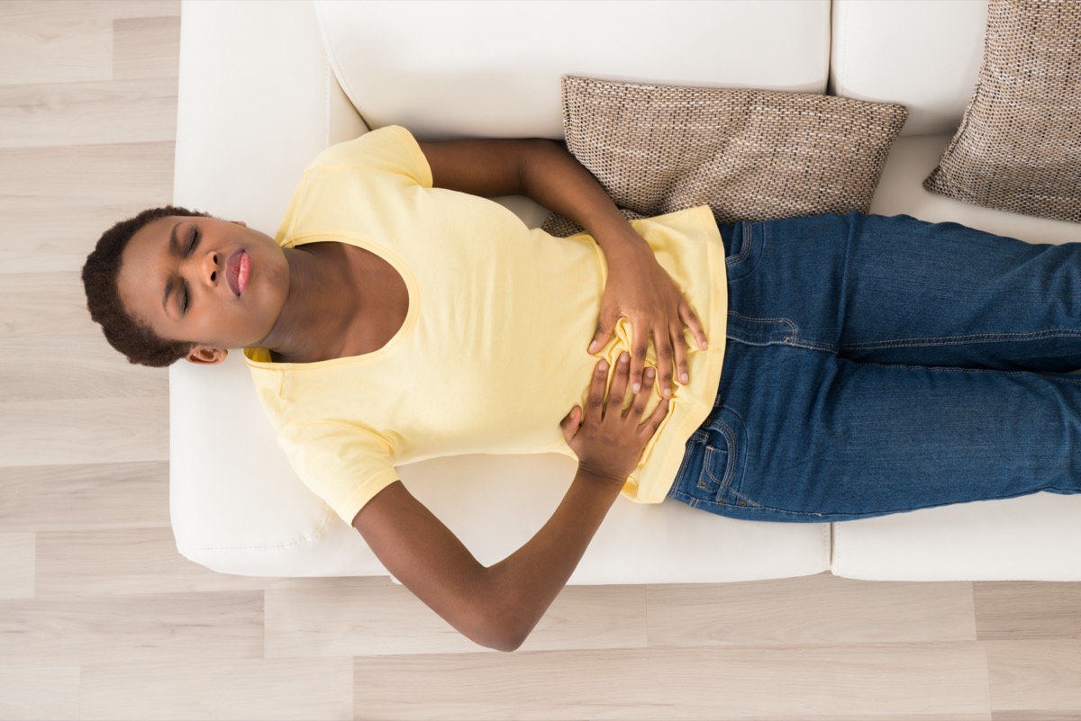 young woman on sofa in yellow shirt and jeans with stomach pain