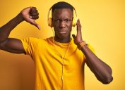 Young man dressed in yellow, listening to music, giving it a thumbs down.