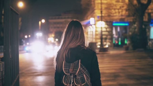 Back view of young woman walking late at night in the city centre