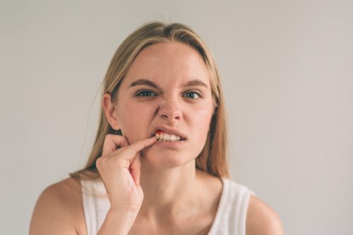 A horizontal photo of a young worried woman looking at her mouth