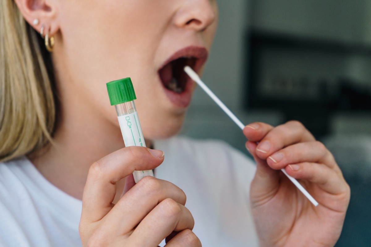 Young woman holds a swab into her mouth and holding a medical tube for the coronavirus / covid19 home test