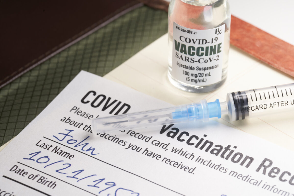 A COVID-19 vaccination record card with a vile of vaccine and a syringe.