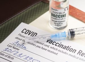 A COVID-19 vaccination record card with a vile of vaccine and a syringe.