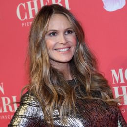 elle macpherson in a shiny gold dress in front of a red step-and-repeat