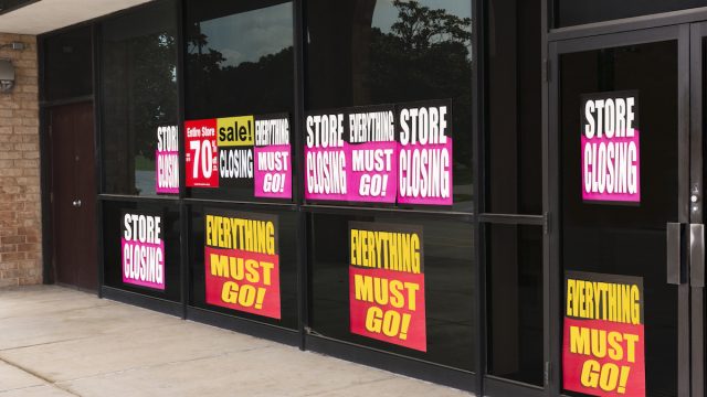 Horizontal angled shot of the windows of a store plastered with going out of business signs