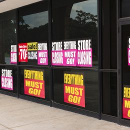 Horizontal angled shot of the windows of a store plastered with going out of business signs
