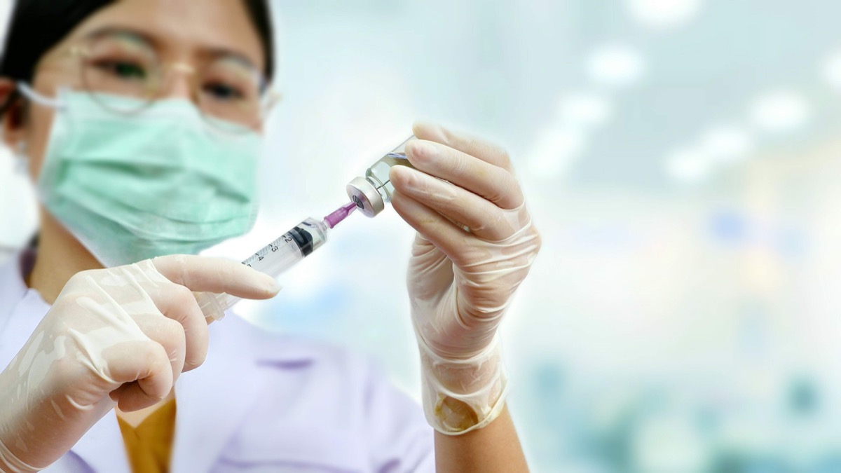 Focus on female doctor's hands holding draw syringe with vial and blurred medical office background, medical health care concept