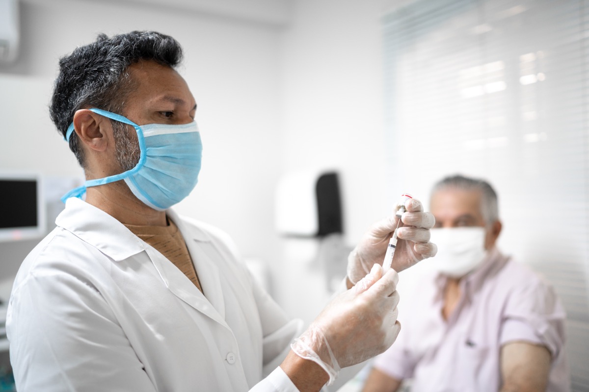 Male nurse preparing vaccine using face mask