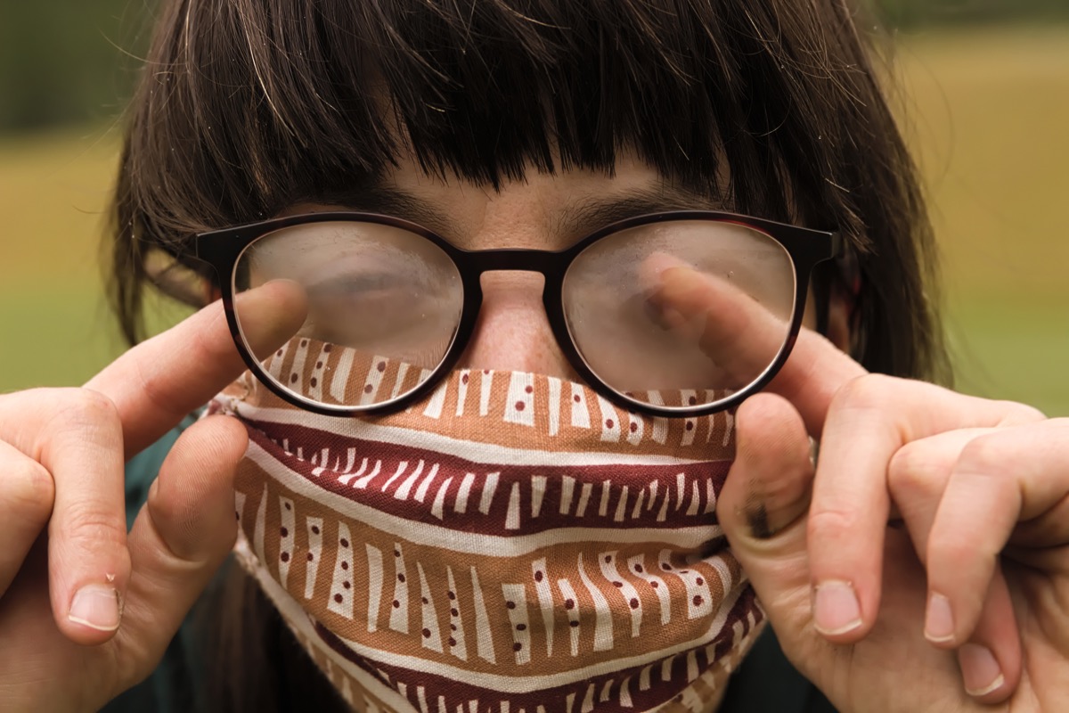Portrait of Young Woman Cleaning her Glasses from Fog when wearing Protective Mask