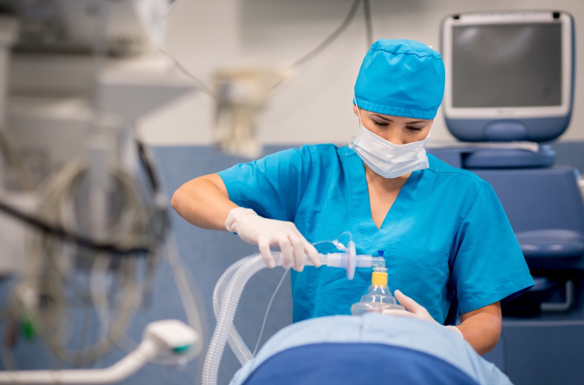 Nurse putting oxygen mask to patient during surgery - healthcare and medicine concepts