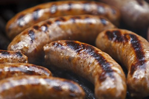 A group of Italian Sausages cook on a grill.