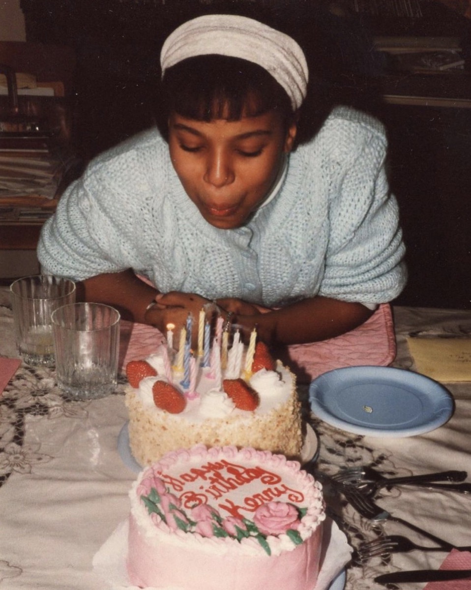 kerry washington in blue sweater and white headband blowing out the candles on a pink or white cake