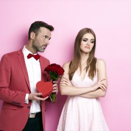 man giving a woman flowers and a heart box and woman looking displeased