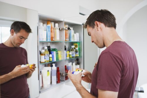 Bărbat care se uită la sticle din dulapul cu medicamente