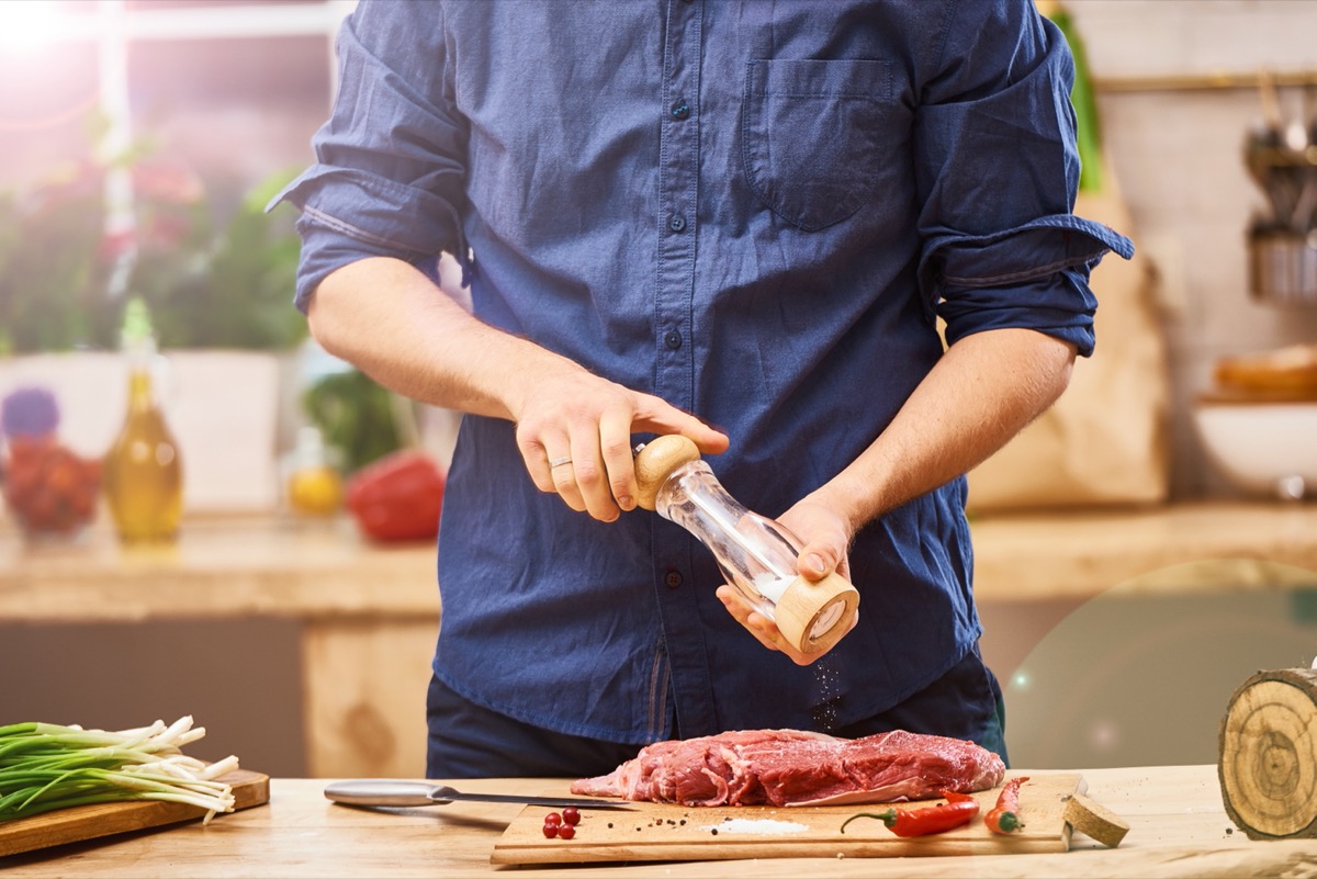 man in blue shirt seasoning a steak or ribs or brisket