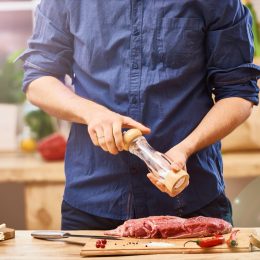 man in blue shirt seasoning a steak or ribs or brisket