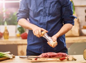 man in blue shirt seasoning a steak or ribs or brisket